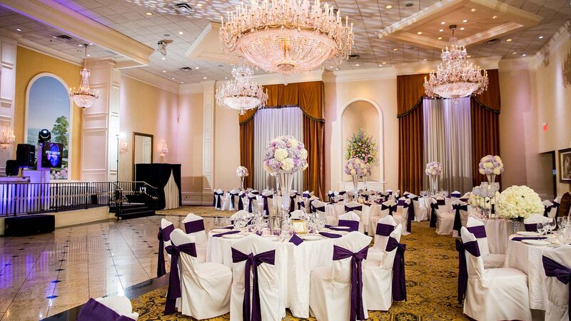Ballroom showing eight tables and flower center pieces. Purple napkins and seat cover accents.