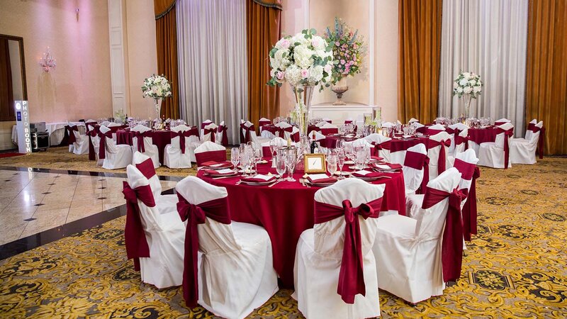Five tables in ballroom. Red napkins, table clothes and chair tie backs. Tables have center pieces.